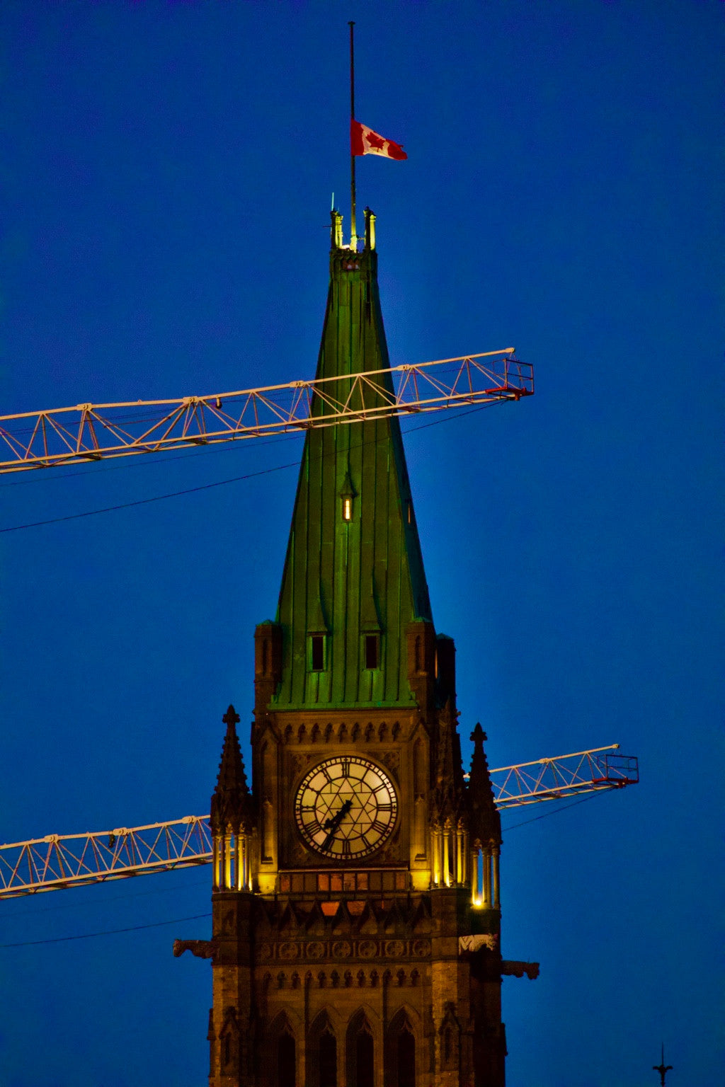 An illuminated clock and cranes against a deep blue sky.